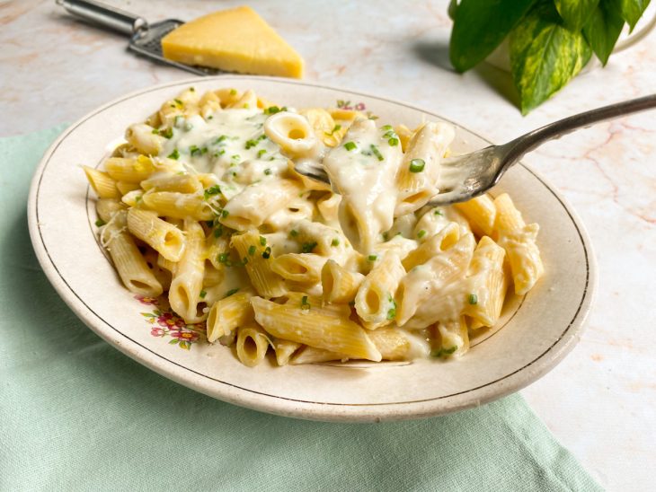 Macarrão com molho branco servido em um prato e decorado com cheiro-verde e parmesão.