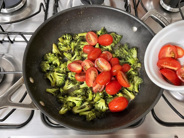 Uma panela com brócolis, manteiga, tomates e temperos ao fogo.