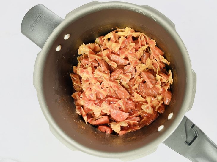 Calabresa refogada, macarrão, molho de tomate e água em uma panela de pressão.