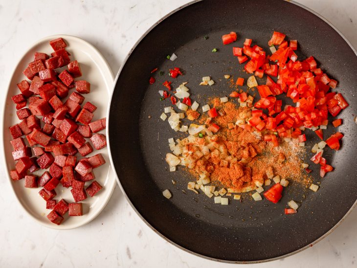 Alho, cebola, tomate, pimenta-de-cheiro, páprica, cominho, sal e pimenta-do-reino em uma frigideira.