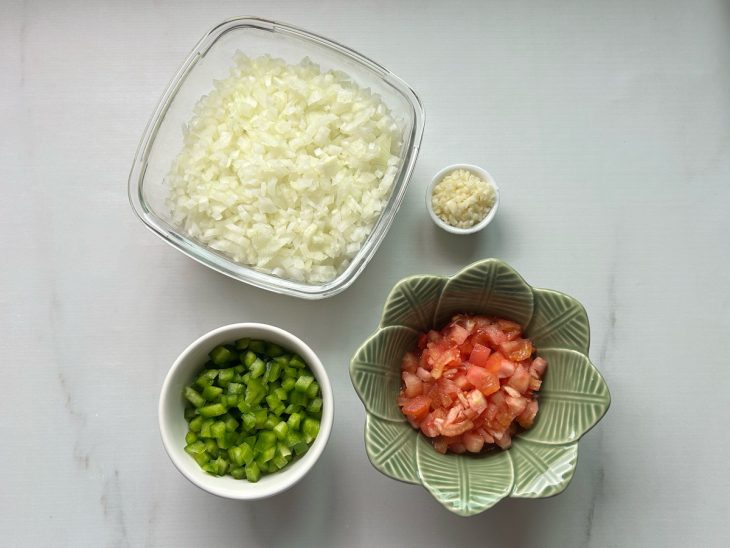 tigela com cebola picada em cubos. Tigela com pimentão cortado em cubos. Tigela com tomate cortado em cubos. Tigela com alho picado