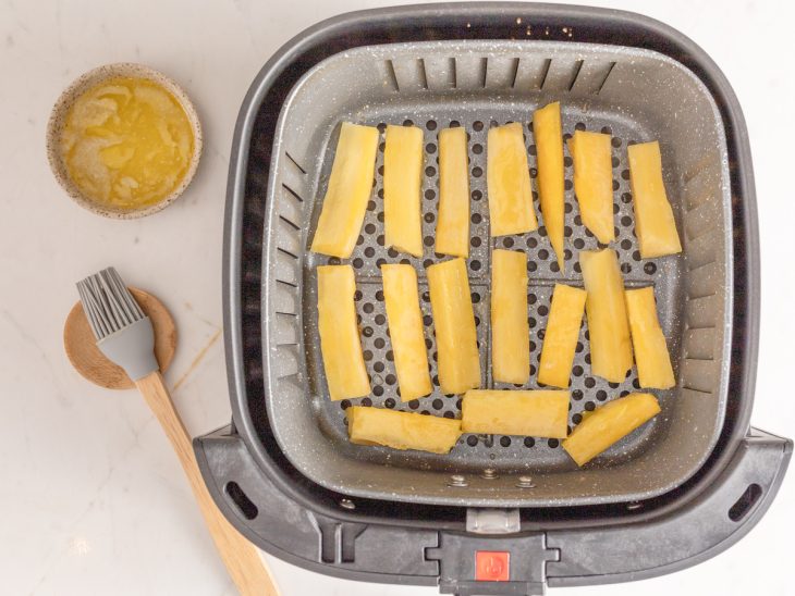 Um cesto de air fryer com pedaços de mandioca.