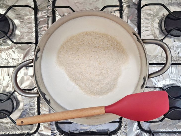 Panela ao fogo com a mistura de leite e amido, com o leite de coco, o açúcar e o coco ralado.