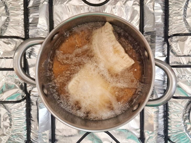 Dois pastéis sendo fritos por imersão em uma panela.