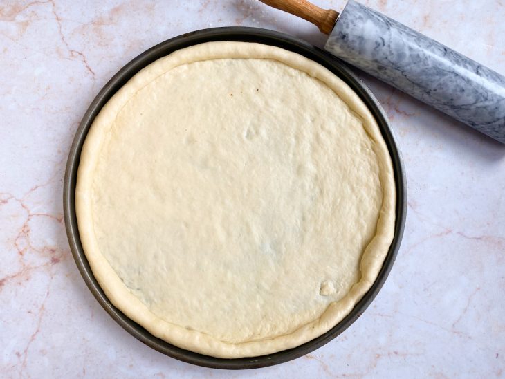 Massa de pizza profissional com as bordas feitas em uma assadeira.