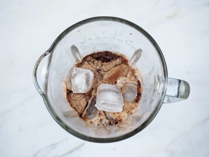 Um liquidificador com cubos de gelo, sorvete, chocolate em pó e leite.