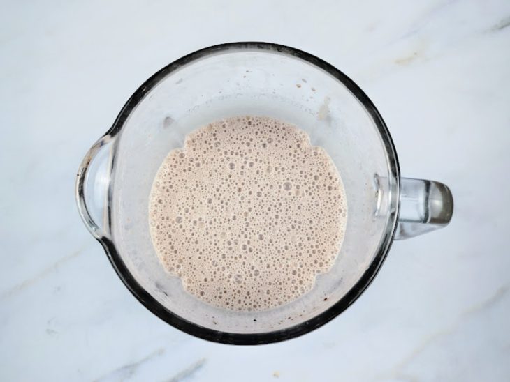 Um liquidificador com cubos de gelo, sorvete, chocolate em pó e leite batidos juntos.