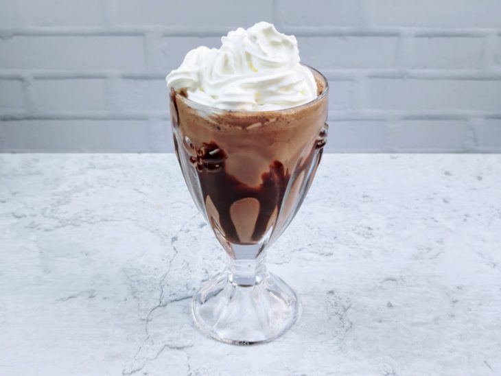 Uma taça com calda de chocolate, milk shake e chantilly.