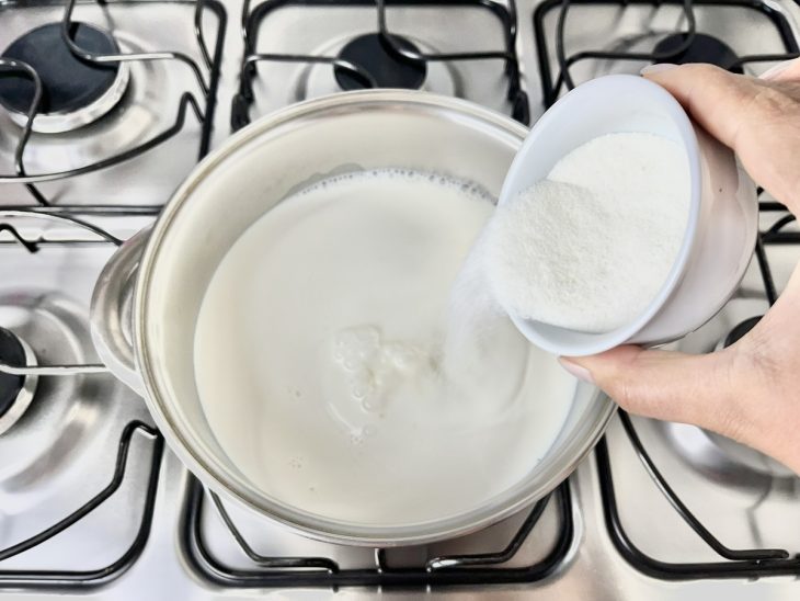 Açúcar sendo adicionado na panela com leite e pasta de Maizena