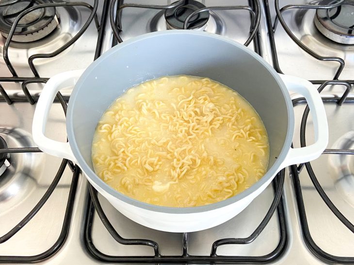 Uma panela com miojo, pasta de queijo, temperos e água ao fogo.