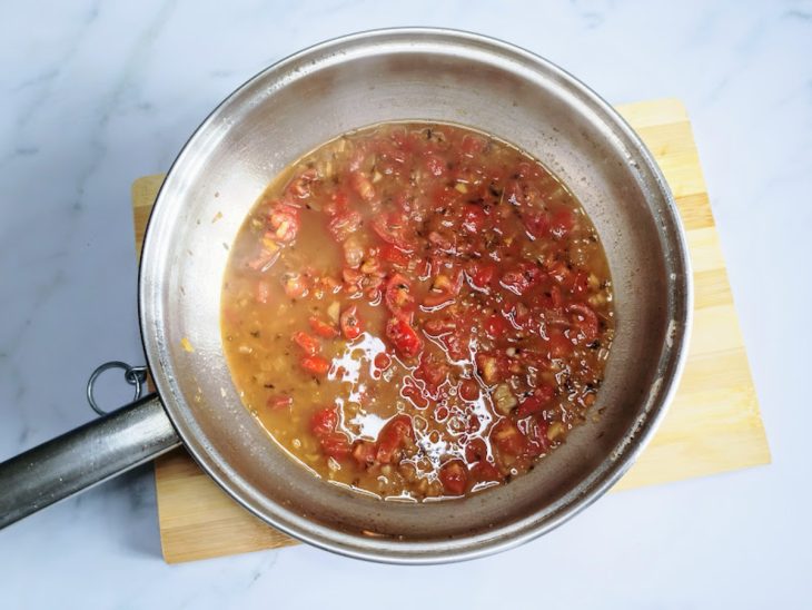 Uma frigideira com alho, cebola, pimenta-do-reino, orégano, tomates-cereja e água.