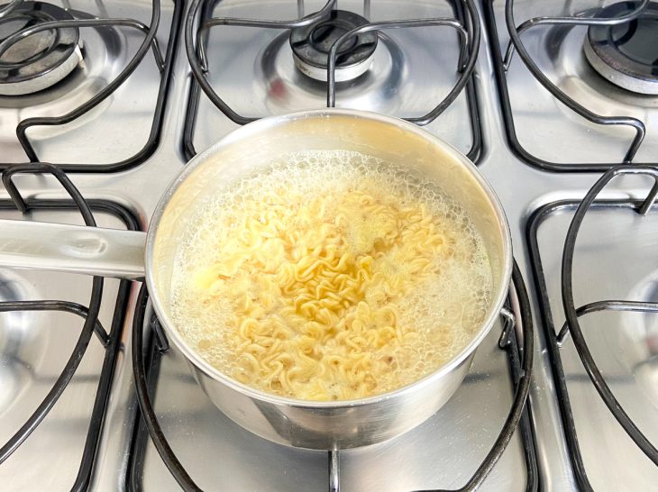 Uma panela ao fogo com o miojo temperado cozinhando.