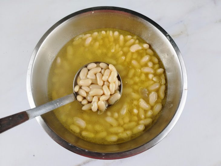 Feijão branco cozido e água do cozimento em um recipiente de alumínio.