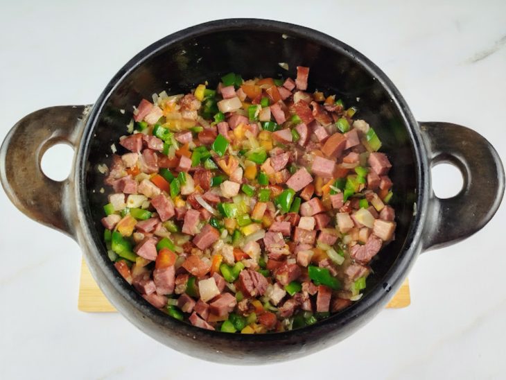 Bacon, calabresa, alho, cebola e pimentão refogados em uma panela.