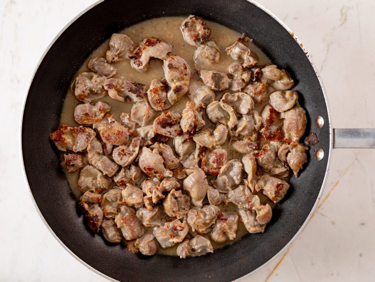 Uma frigideira com moela e temperos cozinhando.