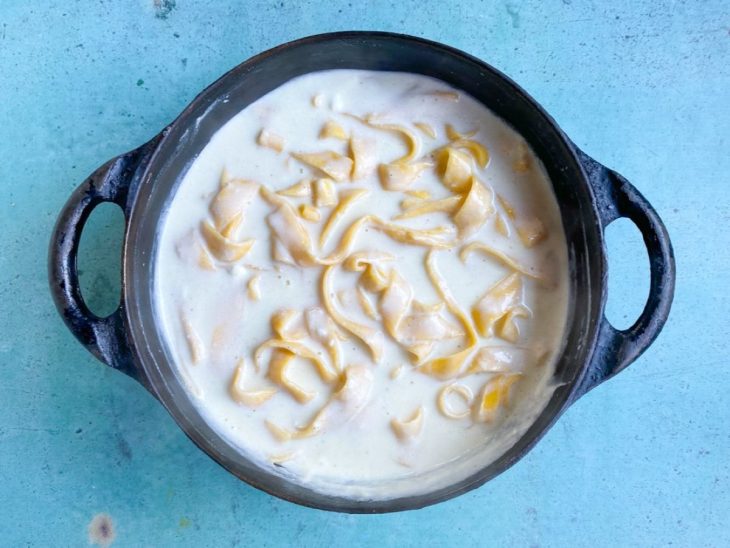 Uma panela com o molho alfredo e o macarrão em processo de cozimento.