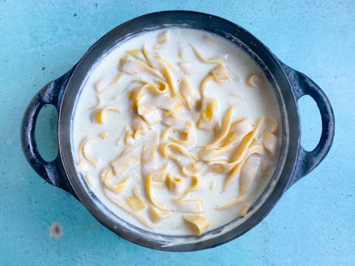 Uma panela com o molho alfredo e o macarrão em processo de cozimento.