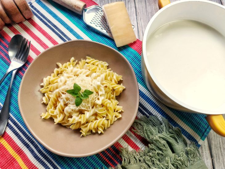 Um prato e uma panela contendo molho branco com creme de leite e queijo.