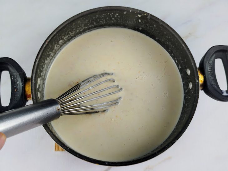 Leite, queijo parmesão, sal e noz-moscada adicionados a panela.