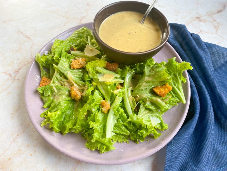 Um prato com salada e um recipiente contendo molho caesar com anchovas.