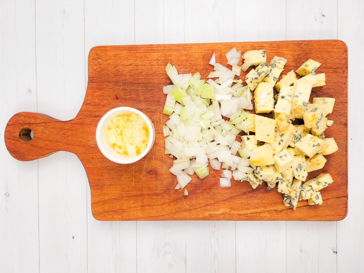 Uma tábua contendo cebolas, alho e gorgonzola picados.