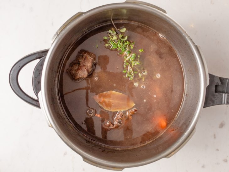 Uma panela com a carne, azeite, mirepoix, vinho e temperos.