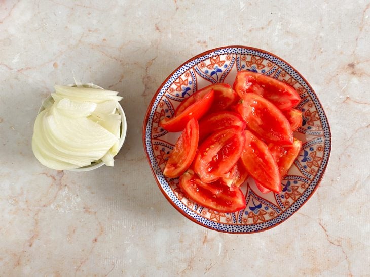 Cebola e tomate em cortes, em recipientes distintos.