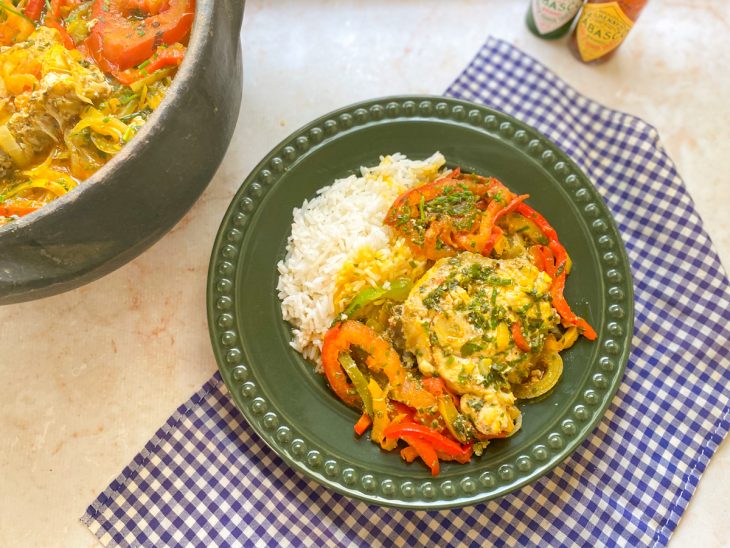 Moqueca de pescada-amarela pronta para consumo, acompanhada por arroz branco em um prato.