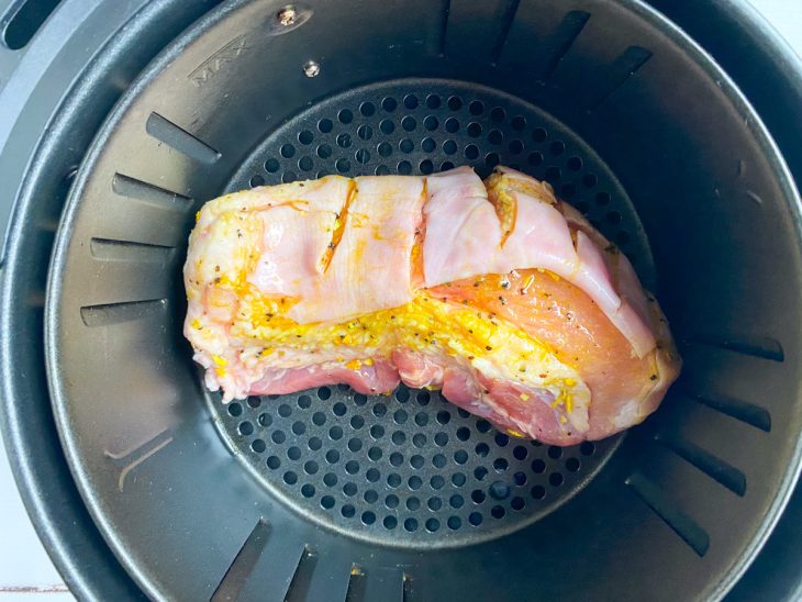 Uma cesta de airfryer contendo panceta temperada.