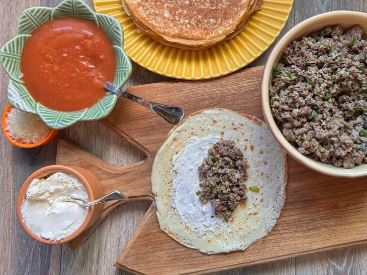 Panqueca sendo recheada com requeijão e carne moída.