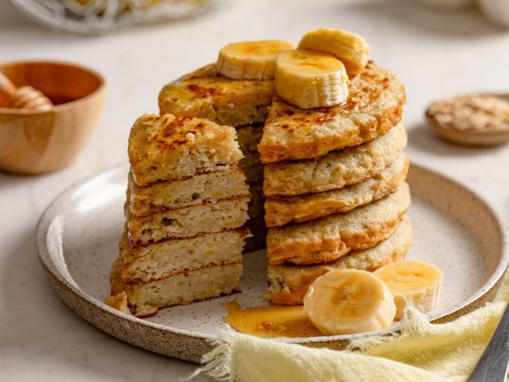 Panquequinhas de banana e aveia prontas para servir, acompanhadas por mel e banana.