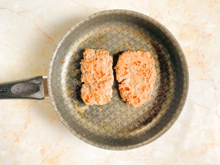 Bifes de linguiça com lados dourados em uma frigideira.