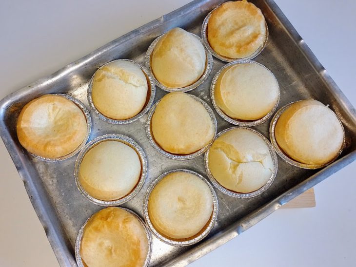 Uma assadeira com forminhas contendo pão de queijo de liquidificador fácil.