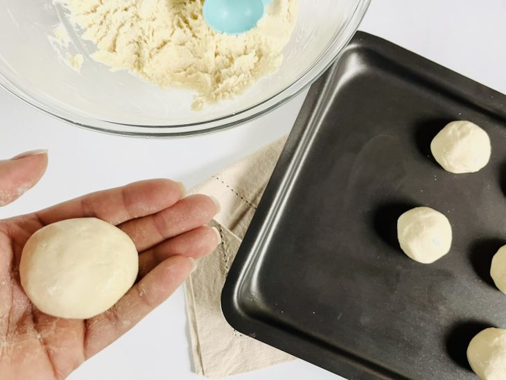 Bolinhas de pão de queijo modeladas e acomodadas em uma assadeira untada.