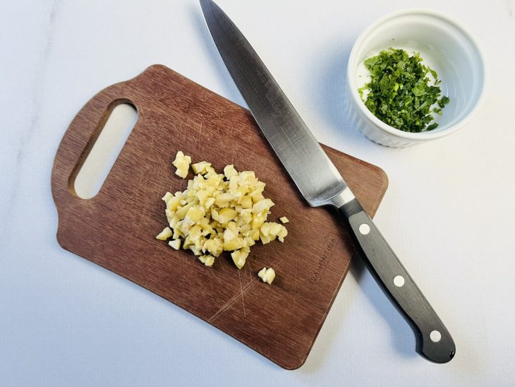 Cheiro-verde picado e reservado em um recipiente próximo à tábua com azeitonas picadas.