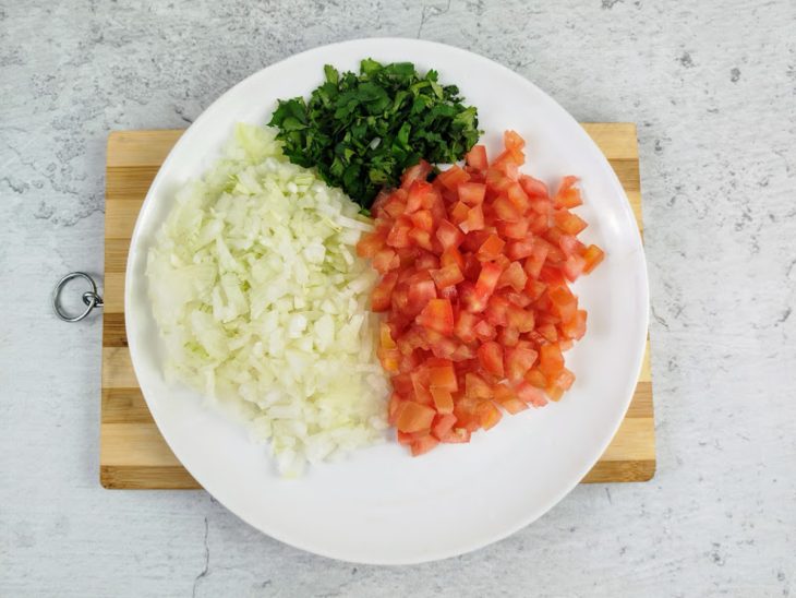 Cebola, coentro e tomate picados em um prato.