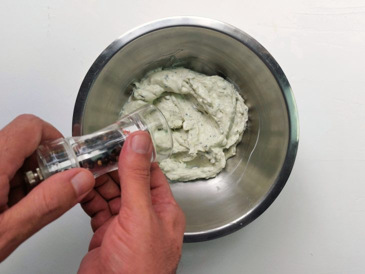 Um recipiente contendo patê de gorgonzola com cream cheese sendo temperado com pimenta.