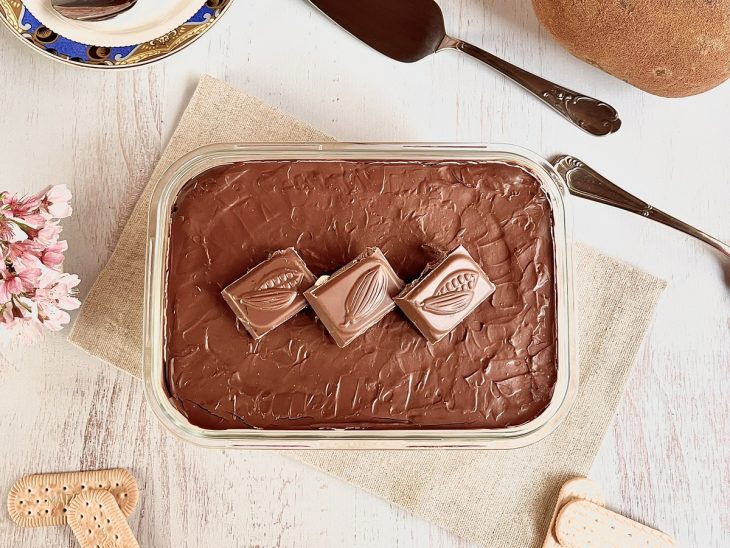 Pavê de cupuaçu decorado com pedaços de chocolate pronto para consumo sobre uma bancada com objetos