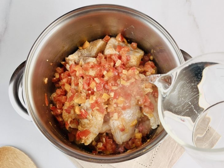 Uma panela com peixe, legumes, temperos e a adição de água.