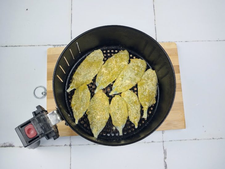 Uma cesta de airfryer contendo peixinhos da horta empanados.