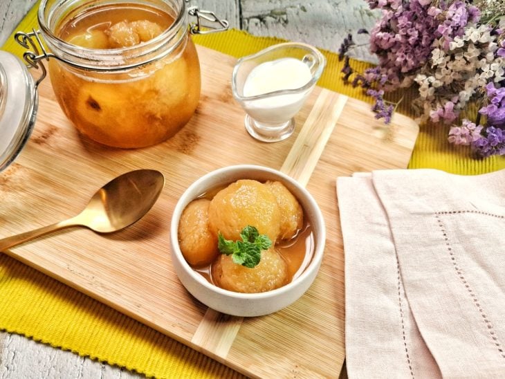 Pêssegos em calda em um pote com um recipiente ao lado com uma porção servida.