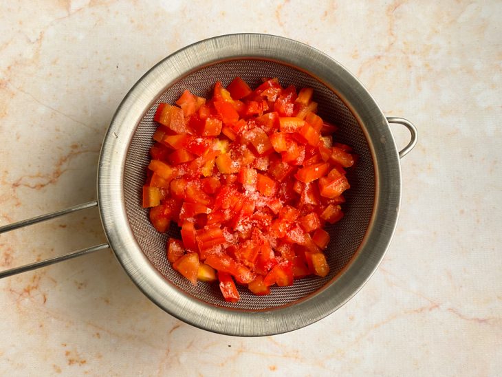 Cubinhos de tomate coados sobre uma peneira e recipiente.