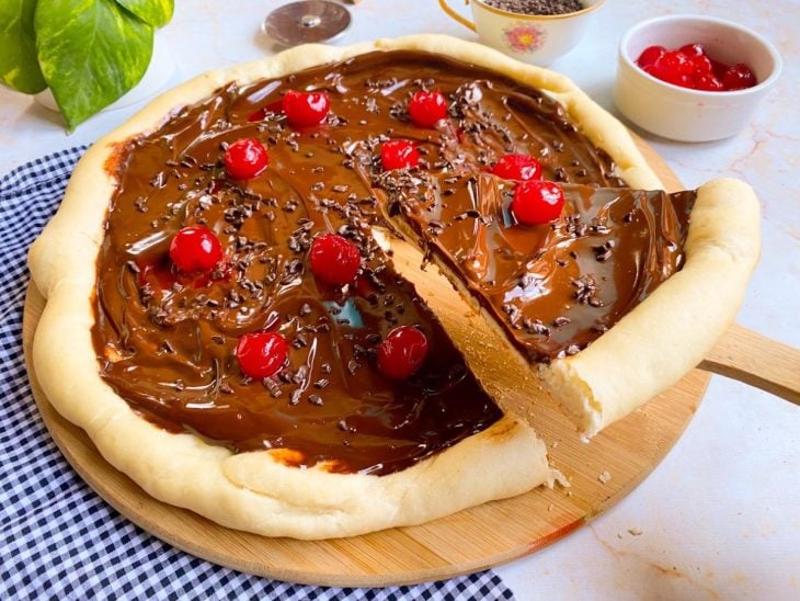 Pizza de chocolate com cerejas em cima como decoração e uma fatia cortada.