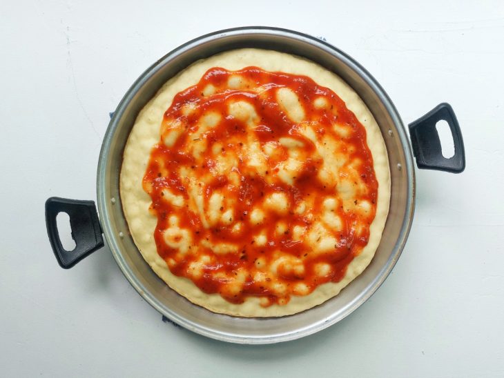 Uma forma com massa de pizza crua e molho.