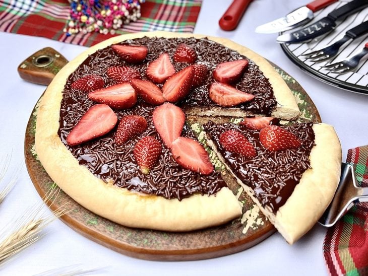 Pizza doce com chocolate e morango com uma fatia cortada.