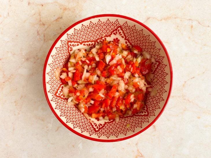 Tomate, cebola, sal e pimenta-do-reino misturados em um recipiente.