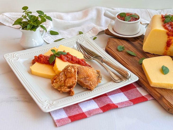 Polenta no fio acompanhada por molho de tomate e manjericão, e frango frito pronta para servir.