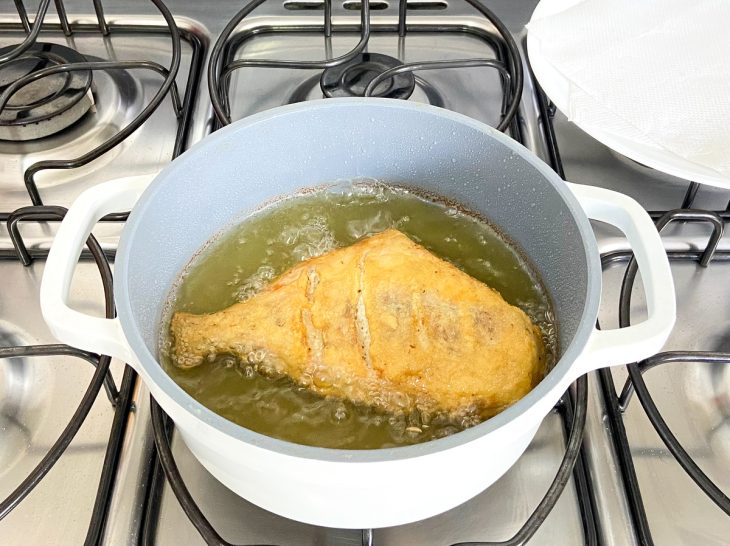 Uma panela contendo 'pleo fritando um peixe porquinho.