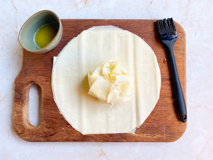 trouxinha de massa com o queijo brie no centro de outro pedaço de massa untada com manteiga derretida.