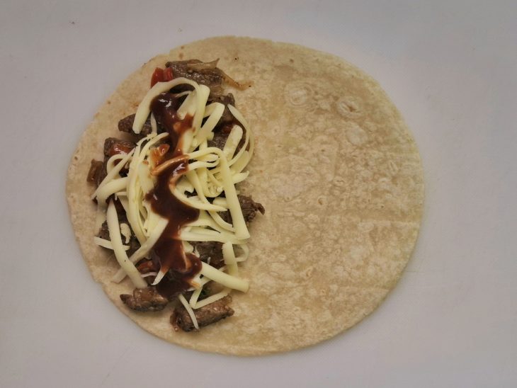 Tortilha com barbecue e mussarela salpicado por cima.